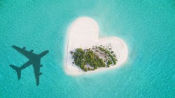 Aerial view of tropical island in heart shape with airplane shadow. Tropical paradise and beach holiday conceptual image.