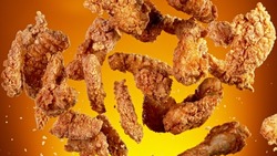 Freeze motion of flying pieces of fried chicken pieces on golden background. Concept of levitating food.
