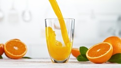 Orange juice pouring into glass. Fresh orange juice with oranges fruit in kitchen. Free space for text. Healthy nad diet concept.