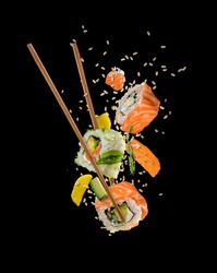 Sushi pieces placed between chopsticks, separated on black background. Popular sushi food.