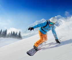 Young man snowboarder running down the slope in Alpine mountains. Winter sport and recreation, leisure outdoor activities.