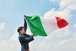man Waving Italian flag against cloudy blue sky, ational holiday of Italy, postcard with patriotic symbols
