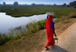 East Indian woman covered in red sari walks to get water for small village.