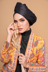 Close up model wearing modern kebaya with black turban, an Asian traditional dress for Muslim woman isolated over beige background. Stylish Muslim female hijab fashion lifestyle concept.