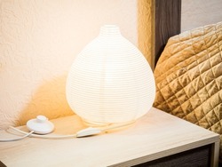 A luminous drop-shaped bedside lamp stands on a light wooden bedside table.
