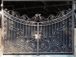 Iron gate with wrought iron monogram pattern in front of a covered private courtyard.