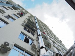 Iron exhaust pipe on the apartment building. Maintenance of apartment buildings. Facade of a high-rise residential building against a cloudy sky. Bottom up perspective view