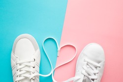 Heart created from white shoelaces between male and female sport shoes. Love concept. Top view. Empty place for lovely, cute text, quote or sayings on pastel blue and pink paper background. Closeup.