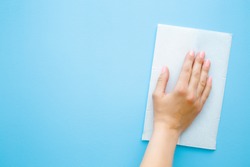 Woman's hand wiping pastel blue desk with white paper napkin. General or regular cleanup. Close up. Empty place for text or logo.