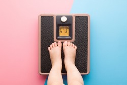 Baby barefoot standing on weight scales on light pink blue floor background. Pastel color. Closeup. Care about body. Children weight control concept.