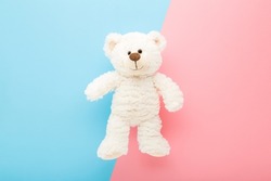 Smiling white teddy bear on light pink blue table background. Pastel color. Closeup. Kids best friend.