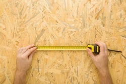 Young adult man hands measuring osb board with measure tape. Closeup. Preparing material for new floor, wall, roof or other places. Home repair work. Point of view shot.