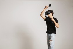 Young man in blank black t-shirt gaming golf or tennis in VR headset hitting someting isolated on white