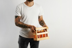 Young man in white cotton t-shirt with tattoos holding a crate of artisan beer isolated on white