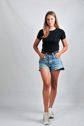 Full length portrait of the beautiful young model in a casual black T-shirt and jeans shorts posing on a grey background