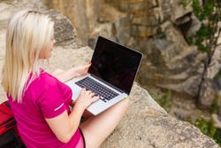 Portrait of a slender young woman on stones near sea. beautiful girl is resting on coast, enjoying outdoor recreation, holding a laptop in her hands, using Internet for business.