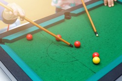 Playing mini billiard, pool game on green table, cue, red and yellow balls, two person playing