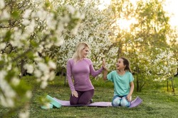 Young sports mother doing physics exercise outdoors in garden near her daughter. Healthy lifestyle. Yoga. Fitness. Family having fun outside. Family spend time together in park.