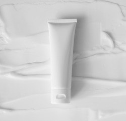 Mockup white plastic tube for moisturizer, lotion, facial cleanser or shampoo on smudged cream texture background top view. Delicate purity skin care product