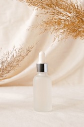 Serum bottle beauty product mockup on linen drapery and dry branch of meadow plant. Concept eco organic cosmetic with natural extracts. Mock up skincare cosmetic product