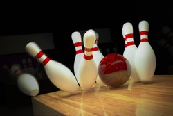 Red bowling ball is making a strike on wooden lane.