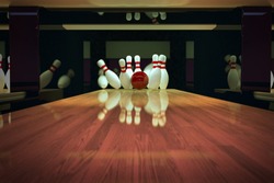 Red bowling ball is making a strike on wooden lane.