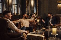 Three men are enjoying drinks in a bar lounge. They are talking and laughing while drinking pints of beer. 