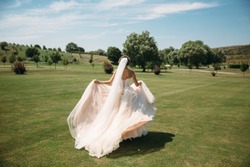 Back view, beautiful bride in luxury fashion white wedding dress with veil on the green golf club glade, wedding day. Amazing full length body portrait of girl. Marriage concept.