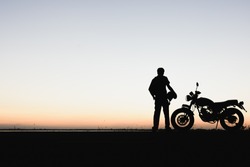 Biker man and motorcycle,Young man rider trendy motorbik had stopped to rest during the trip to see the light of nature,light of the sky between change day to night. silhouette wallpaper concept