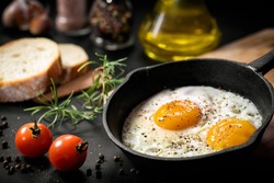Fried eggs in a frying pan with cherry tomatoes and bread for breakfast on a black background.