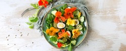 flat lay plate of salad with eggs, cucumbers and edible nasturtium flowers on light wooden table, space for text