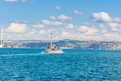 Naval vessel passing though Bosphorus  Bridge with background of Bosphorus strait on a sunny day with background cloudy blue sky and blue sea in Istanbul, Turkey. Blue Turkey concept.