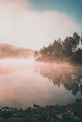 Misty morning at a lake in Norway during sunrise with fog.