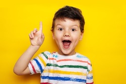 idea. child, boy emotionally points up. A gesture of an idea. Portrait of a child in a bright striped T-shirt on a yellow background, studio