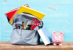 Backpack with school tools and piggy bank on turquoise background
