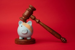 Broken pink piggy bank with beige adhesive with wooden judge gavel on a red background. Law and bankruptcy concept
