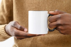 Ceramic mug mockup. Close up african-american hands holding white cup with black handle of coffee, copy space. Front view, space for branding imprint