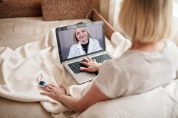 Old woman in bed looking at screen of laptop and consulting with a doctor online at home, telehealth services during lockdown, distant video call, modern tech healthcare application