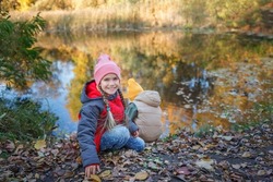 Happy two siblings have rest on the bank of river. Magnificent view of the autumn forest and its reflection in the lake water. Autumn walk. Outdoor lifestyle, active family lifestyle, view from behind