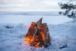 Family winter picnic. Bonfire on the shore of a frozen lake during a winter family walk in the forest, outdoor family weekend at snowing day, winter travel