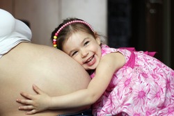 Happy kid girl hugging pregnant mother's belly, pregnancy and new life concept