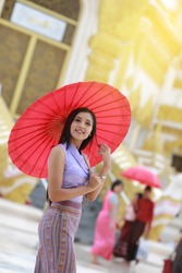 Cute Burmese women with traditional  Burma dress holding red umbrella walk in temple 