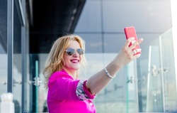 A successful woman entrepreneur in a magenta jacket makes a selfie on the terrace of a cafe in a business center. Business woman representation concept