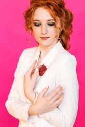 A red brooch in the shape of an anatomical heart on a red-haired girl's white jacket. The girl poses on a bright pink background. Vertical photo.