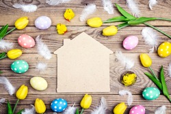 Home symbol with Easter eggs, chickens and yellow tulips on old wooden background. Space for text. Top view.