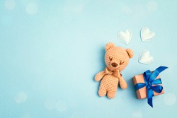Toy bear and gift box on a blue background with copy space. Greting card concept. Top view, flat lay.