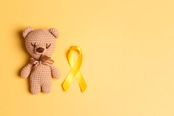 Children's toy with a Childhood Cancer Awareness Yellow Ribbon on yellow background. Childhood Cancer Day February, 15.