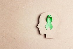 World mental health day concept. Green awareness ribbon with brain symbol on a brown background. Copy space for text.