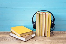 Audio book concept, yellow cover book and headphones over blue wooden background.
