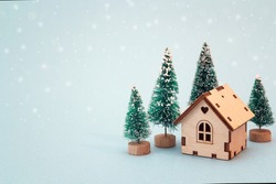 Christmas and New Year miniature  house with fir trees on blue background. Copy space for text. Winter card. Holiday and celebration concept. 